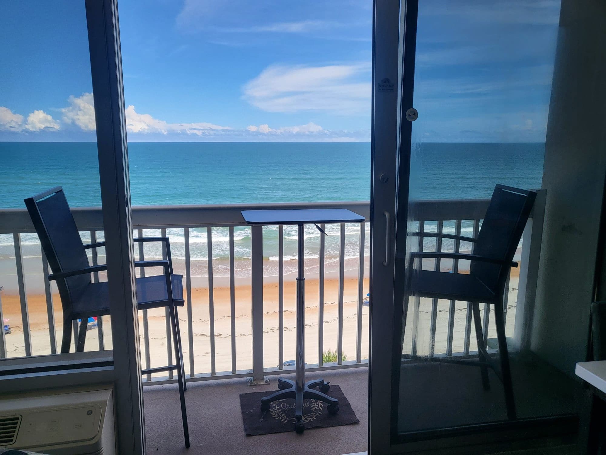 A balcony with a view of the ocean, two chairs, and a small table.