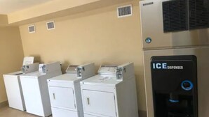 Een wasruimte met vier witte wasmachines en een ijsmachine in het zwart.