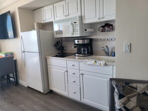 A compact kitchen with white cabinetry, a refrigerator, a microwave, a coffee maker, and a sink. - Surf N Sun spectacular oceanfront studio w/balcony (Daytona Beach)