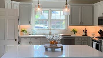 A modern kitchen with white cabinetry, a central island with a glass bowl, pendant lights, and a window providing natural light.