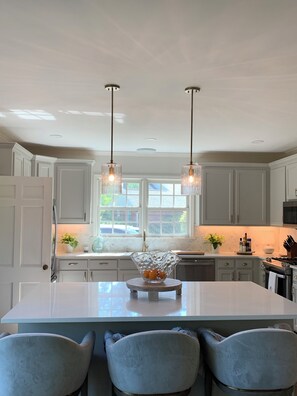 A modern kitchen with white cabinetry, a central island with a glass bowl, pendant lights, and a window providing natural light. - Spacious, Fully Renovated Sumter Home Near CCTC, USC Sumter & Prisma Health (Sumter)