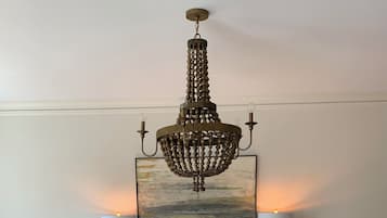 A dining area with a round wooden table, six chairs, a chandelier, a painting, and two wall-mounted lamps.