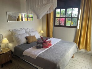 A neatly made bed with a canopy, a bedside lamp, and a window with curtains. - Pearl of the Ocean: Ocean View (Les Anses-d'Arlet)