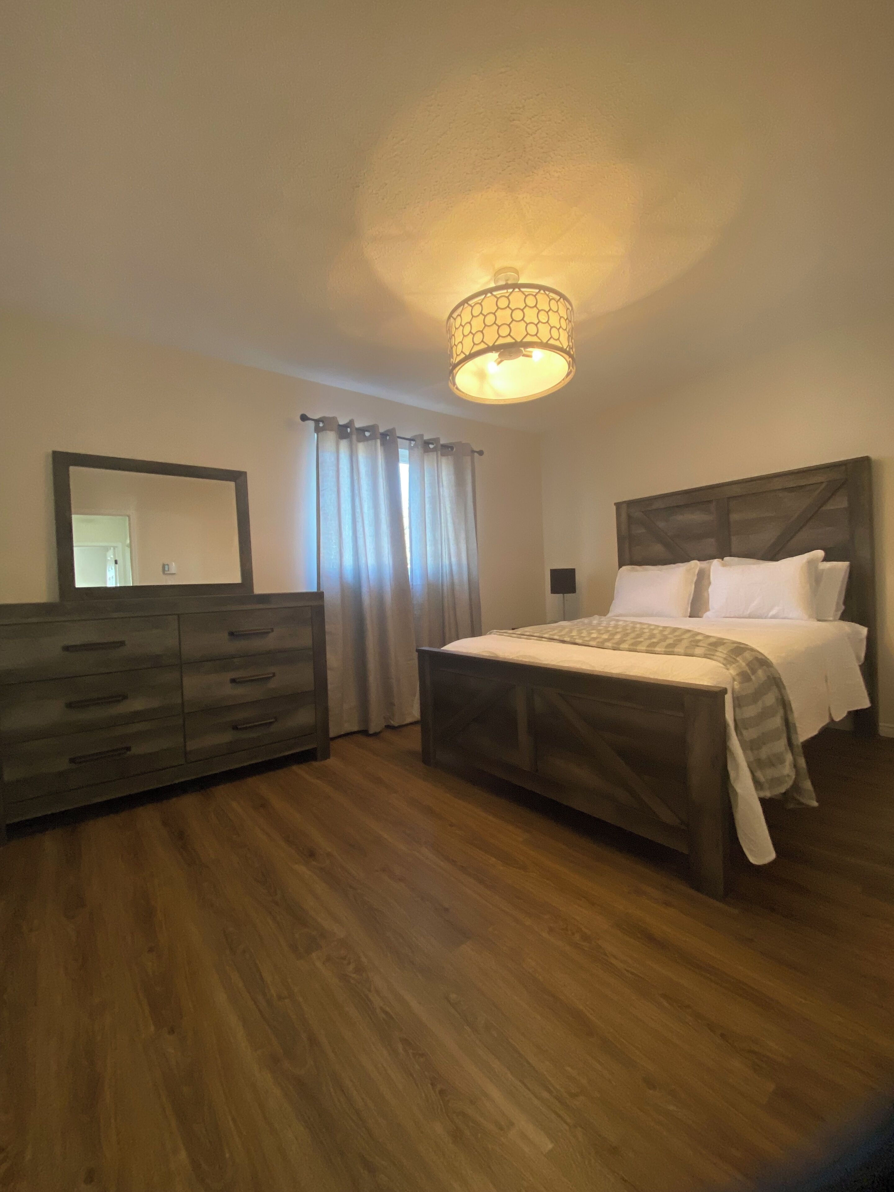 Ein Schlafzimmer mit einem hölzernen Bett, einem Schminktisch, einem Spiegel und einer Deckenleuchte.