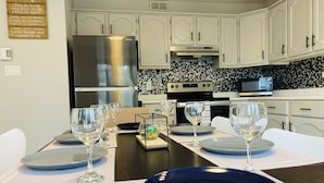 A modern kitchen with white cabinetry, a stainless steel refrigerator, a microwave, and a tiled backsplash.