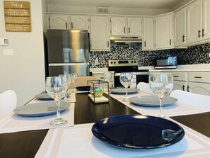 A modern kitchen with white cabinetry, a stainless steel refrigerator, a microwave, and a tiled backsplash.