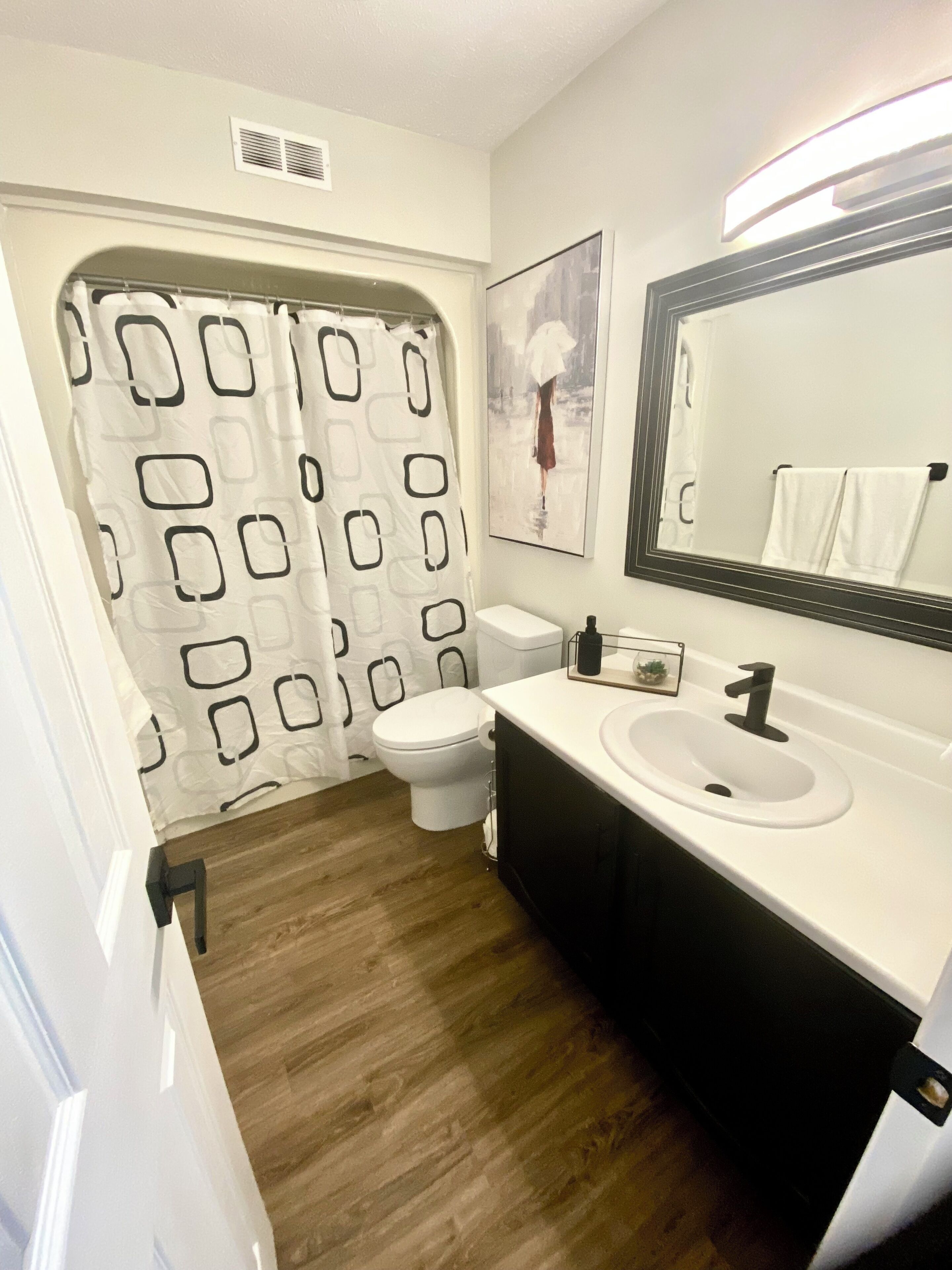 A bathroom with a shower curtain, toilet, sink, and mirror.