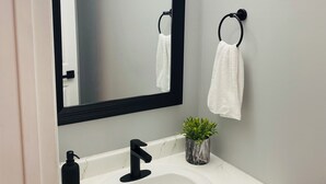 A bathroom with a white sink, a black faucet, a mirror with a black frame, a towel ring, and a small potted plant.