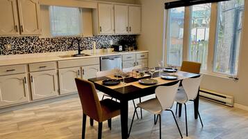 A modern kitchen with a dining area, featuring a tiled backsplash, wooden cabinets, and a large window with a view.