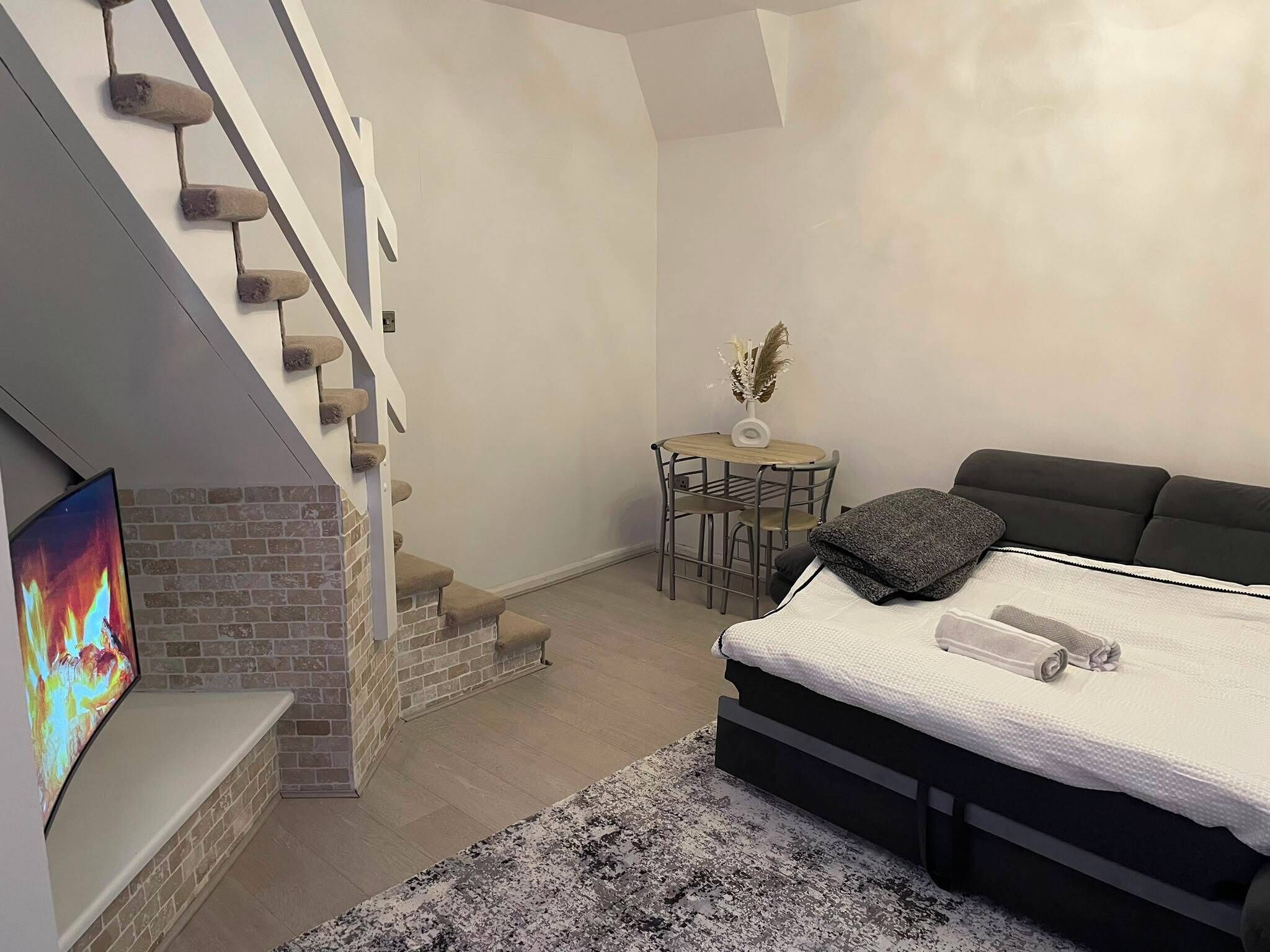 A modern living room with a fireplace, a sofa, a dining table, and a staircase.