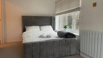 A bedroom with a bed, a window with blinds, a radiator, and a small plant on the windowsill.