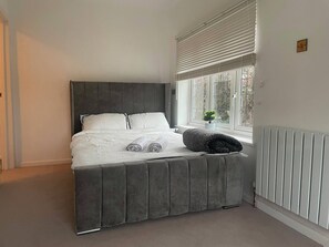 A bedroom with a bed, a window with blinds, a radiator, and a small plant on the windowsill. - Cosy cute modern square (Watford)