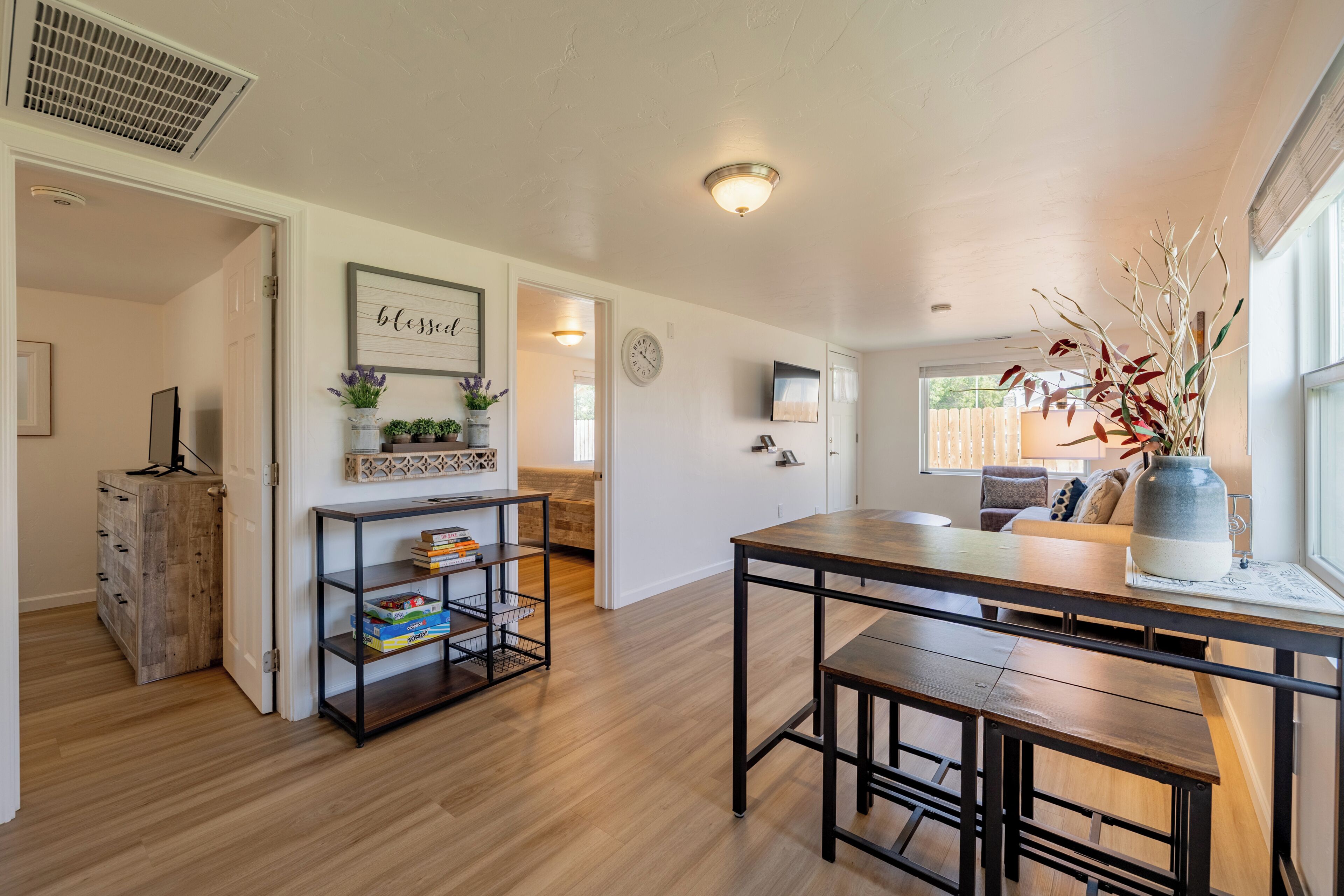 A spacious living area with a wooden dining table, a bookshelf, and a decorative vase.