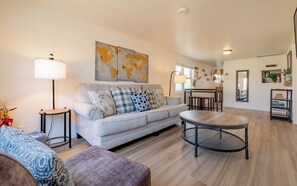 A living room with a sofa, a round coffee table, and a world map artwork on the wall. - Newly remodeled downtown Bleistein cottage 2bd/1 bath w/AC - sleeps up to 5! (Cody)