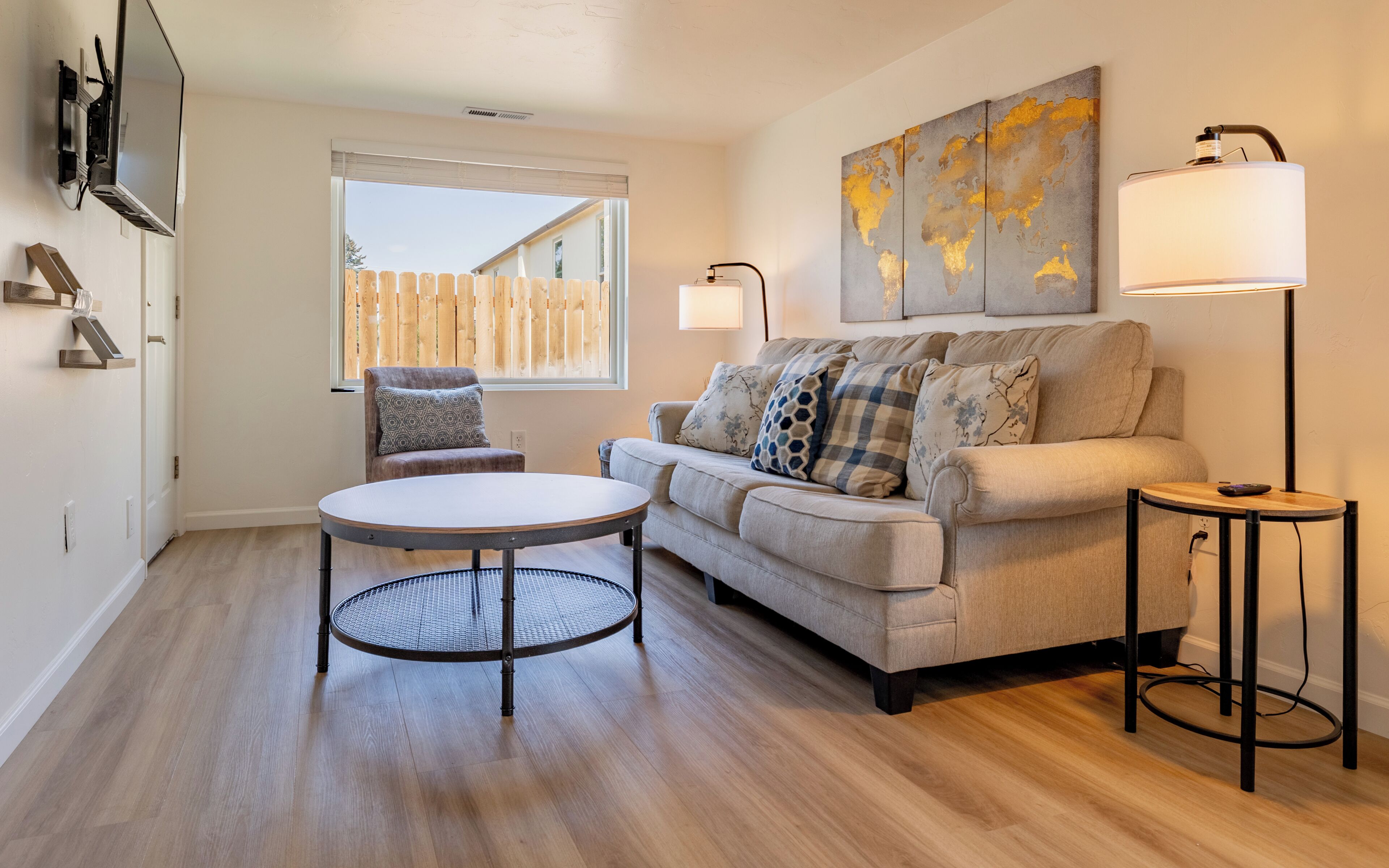 Un salon comprenant un canapé, une table ronde, une chaise, un lampadaire et un téléviseur fixé au mur.
