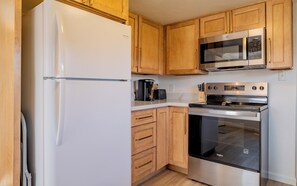A kitchen with wooden cabinets, a stainless steel refrigerator, a microwave, and an oven. - Newly remodeled downtown Bleistein cottage 2bd/1 bath w/AC - sleeps up to 5! (Cody)