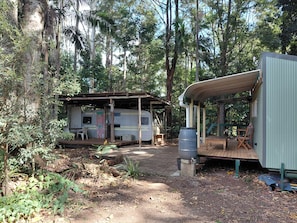Um acampamento arborizado com uma carrinha e uma pequena estrutura de madeira.