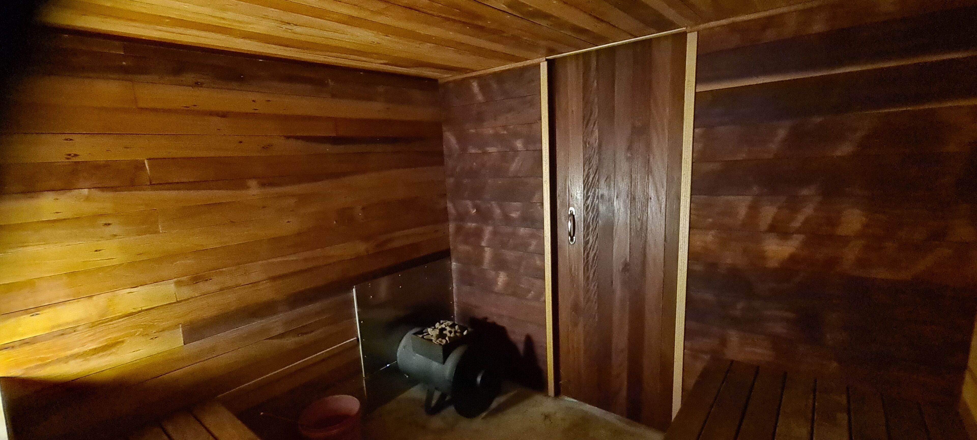 A wooden interior with a door, a small window, and a trash bin.