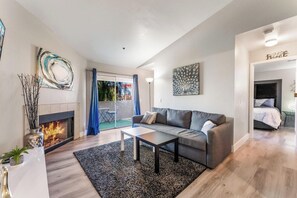 A modern living room with a fireplace, a grey sofa, a coffee table, and a view of the outside. - Luxury 2BR/2BA Condo - Walk to the Strip, Rio & Palms! (Las Vegas)