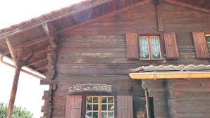 A rustic wooden building with a sign that reads 'LE NID DES PERDIX'. - Outside: Apartment located on the ground floor of a chalet, with private garden, outdoor furniture a (St-Luc)