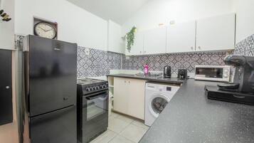 Una cocina compacta equipada con refrigerador, horno, microondas y lavadora.