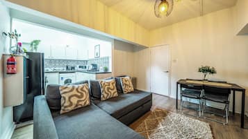 Una sala de estar moderna con un sofá gris, una mesa de comedor con sillas y una cocina al fondo.
