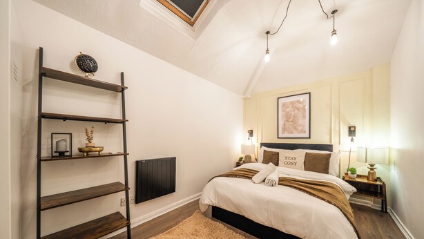 Un dormitorio con cama, mesitas de noche, estantería, radiador y una alfombra mullida.