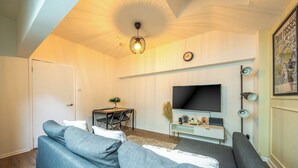 Una sala de estar con sofá, televisor, una mesita con sillas y una lámpara de techo.