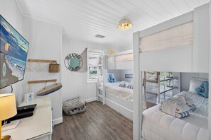 A bedroom with bunk beds, a desk with a lamp, a wall-mounted TV, and a decorative turtle sign. - Sugar Magnolia! Beach Front, Private Pool, Free Beach Gear! (St. George Island)