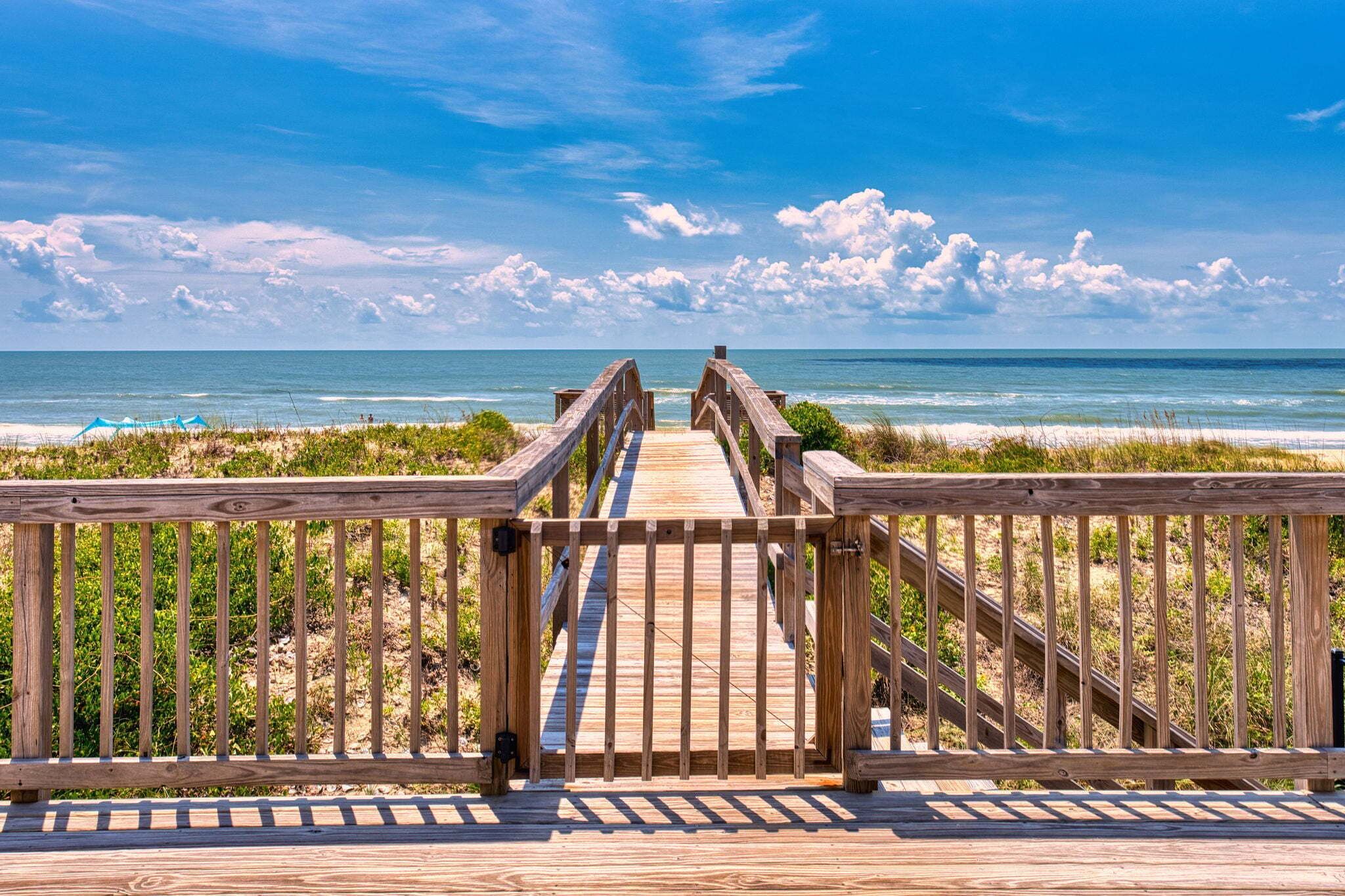 A wooden boardwalk leading to a beach with a clear view of the ocean.