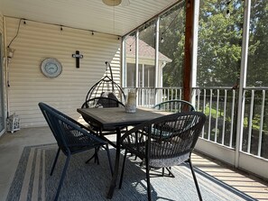 A covered outdoor seating area with a table and chairs, a clock, and a railing overlooking a residential area.