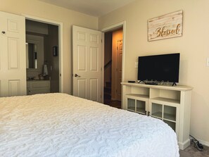 A bedroom with a bed, a television on a stand, and a door leading to a hallway.