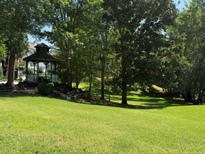 A gazebo in a grassy park area with trees.