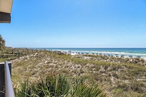 A beach with a wooden walkway leading to the shore, a sandy beach area with blue umbrellas, and the ocean in the background. - Gulf Front Condo w Pool, Tennis Courts & more! (Fort Walton Beach)
