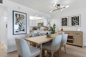 A modern kitchen with white cabinets, a microwave, and a dining area with a wooden table and grey chairs. - Gulf Front Condo w Pool, Tennis Courts & more! (Fort Walton Beach)