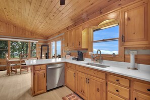 A modern kitchen with wooden cabinets, a stainless steel dishwasher, and a large window offering a view of the outdoors.