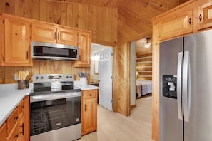 Eine Küche mit Holzausstattung, einem Edelstahlkühlschrank, einer Mikrowelle und einem Herd.