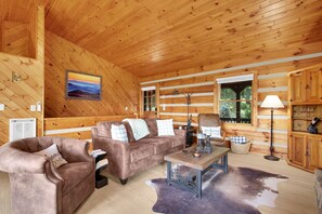 Ein gemütliches Blockhaus-Interieur mit Holzbalkendecke, einer Sofaecke, einem Couchtisch und einem Kamin.