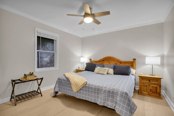 A bedroom with a bed, a nightstand, a bedside table, a ceiling fan, and a window with blinds.