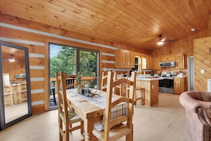 Ein Holzblockhaus-Innenraum mit Essbereich, Küche und großen Schiebeglasfenstern zu einer Außenterrasse.