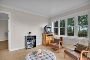 A room with a wooden cabinet, a gaming console, a sofa, and a window with a view of trees.