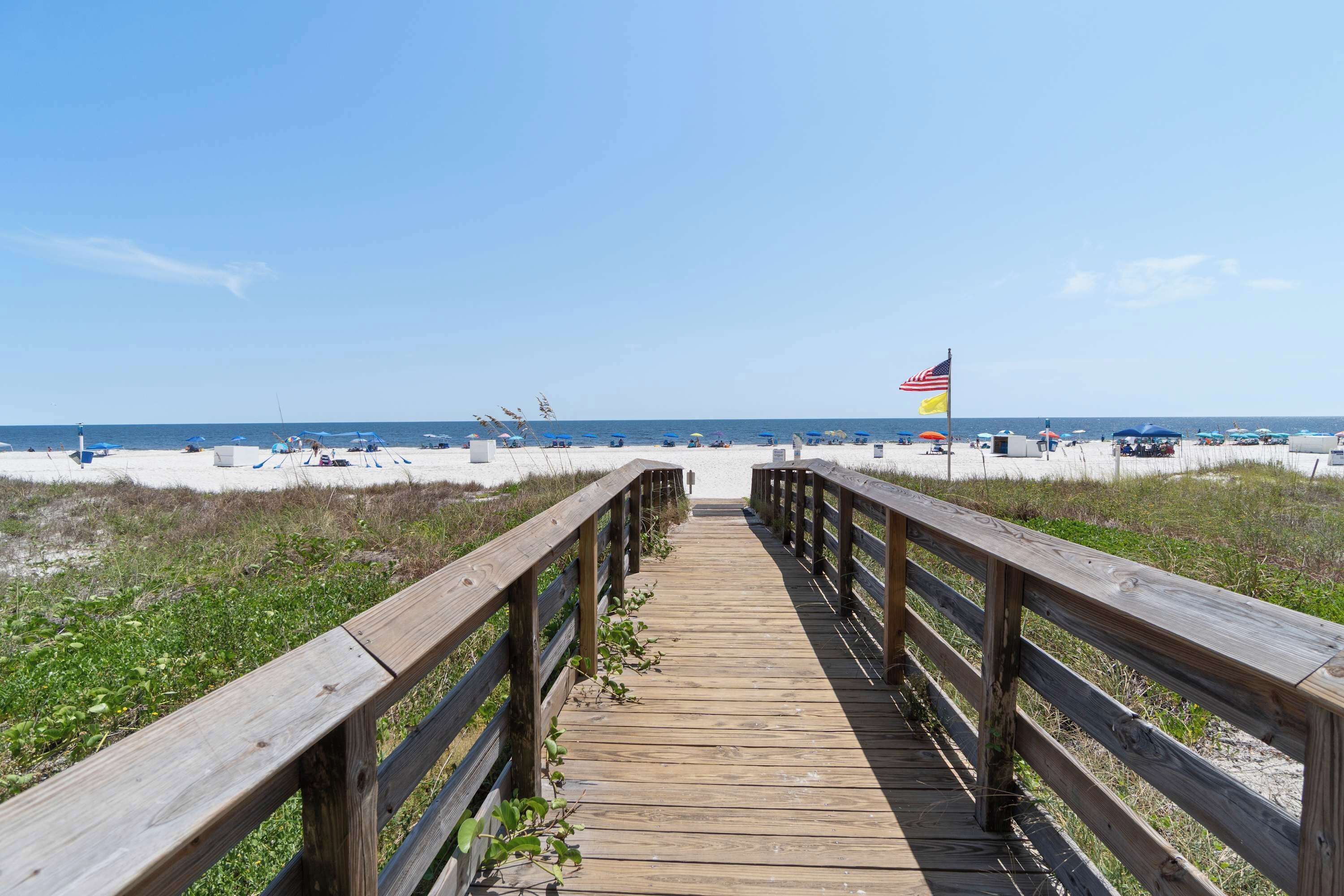 Ein hölzerner Steg führt zu einem Strand mit einer Flagge.