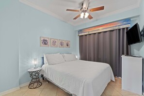 Ein Schlafzimmer mit einem Bett, einem Nachttisch, einem Deckenventilator, einem Fernseher und Kunstwerken an der Wand.