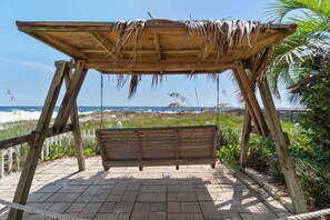 Eine Holzbank unter einem Reetdach mit Blick auf Strand und Meer.