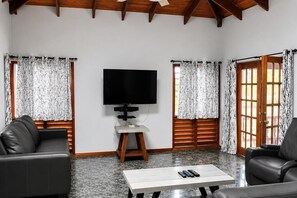 Ein Wohnzimmer mit Flachbildfernseher, zwei Ledersofas, einem Couchtisch und gemusterten Vorhängen.