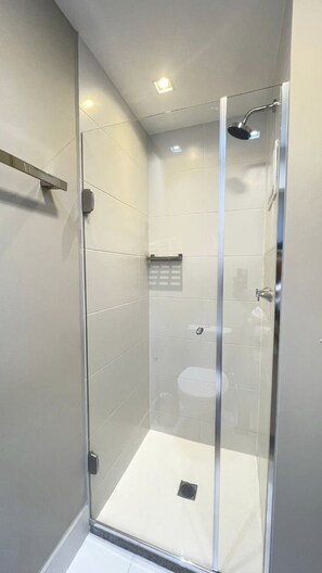 A modern shower with a glass door, a handheld showerhead, and a visible drain. - Estúdio Charme Urbano - Consolação (São Paulo)