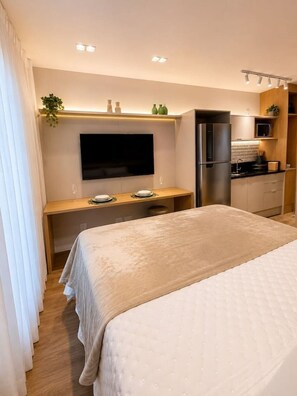 Ein Hotelzimmer mit einem Bett, einem Schreibtisch, einem Flachbildfernseher, einem Kühlschrank und einer Küchenzeile.