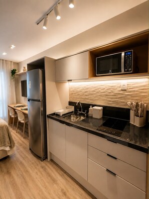 A modern kitchen with a stainless steel refrigerator, a microwave, a sink, and a countertop with a knife block. - Estúdio Charme Urbano - Consolação (São Paulo)