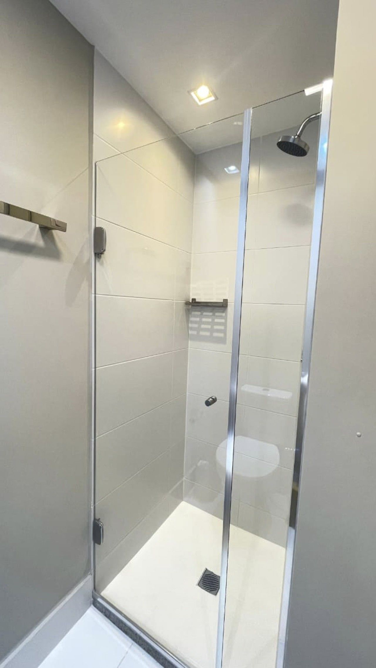 Een moderne douchecabine met een glazen deur, een handdouche en een handdoekhouder.