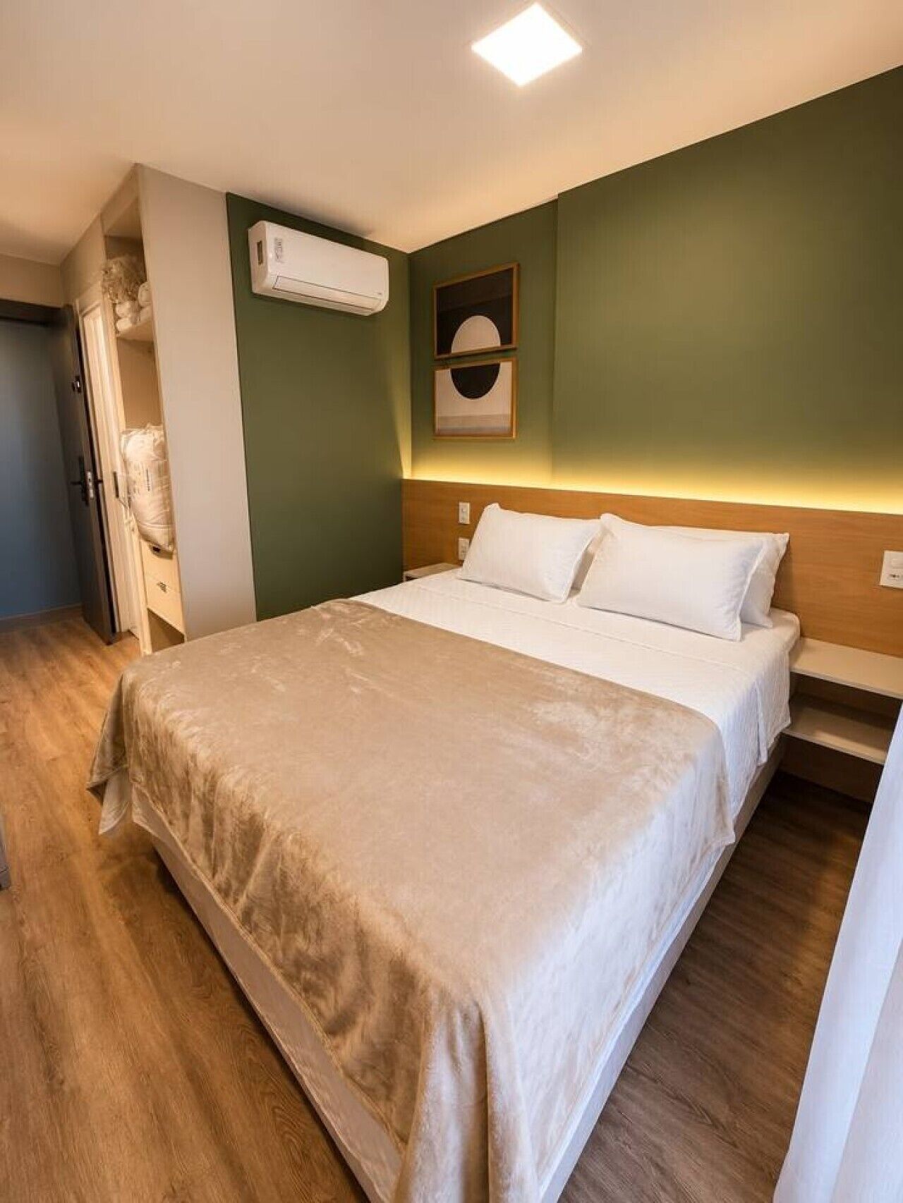 A hotel room with a bed, a nightstand, a wall-mounted air conditioner, and a door leading to a closet.